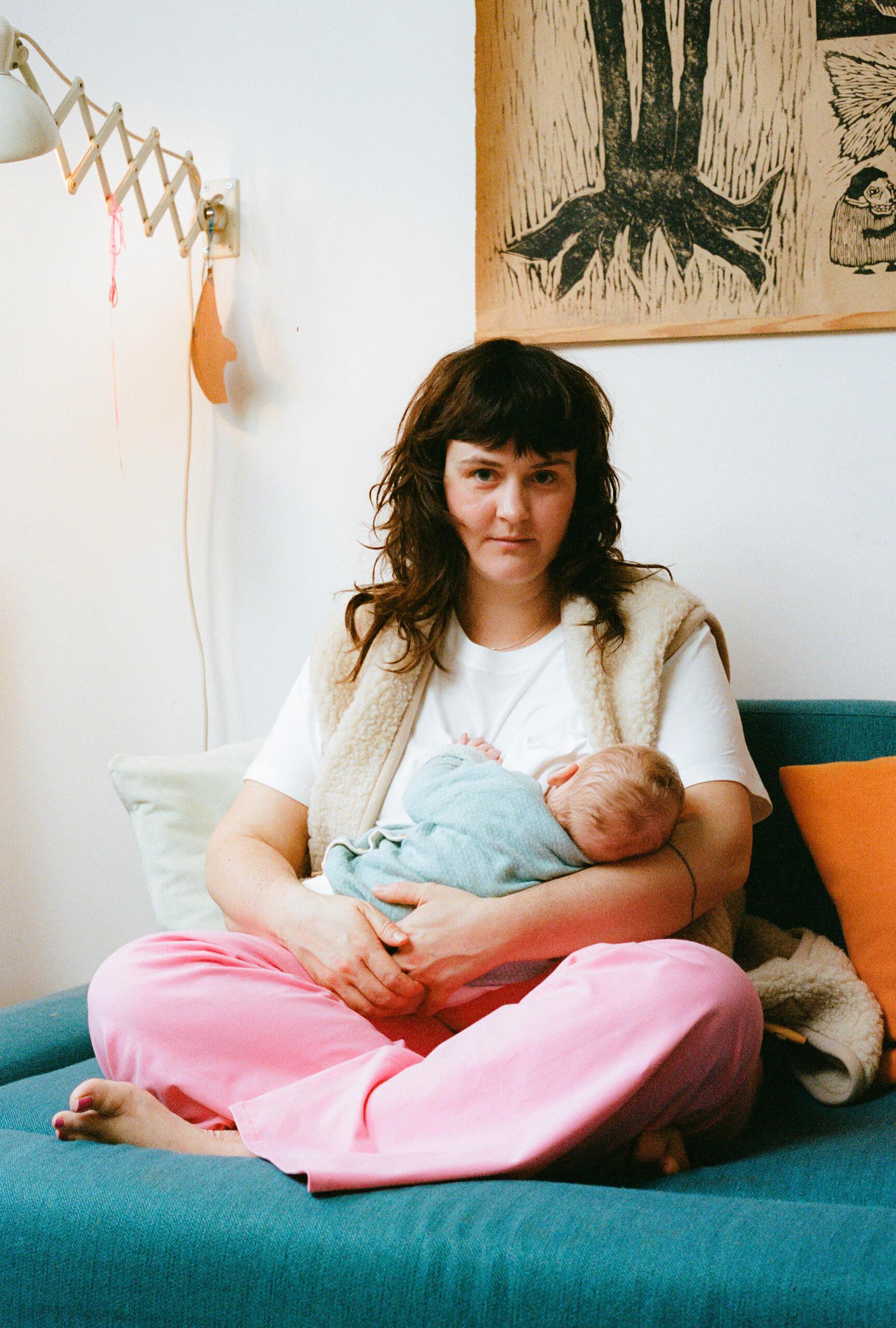 Greta stillt ihr Neugeborenes Mutter stillt ihr Baby, trägt nachhaltige Umstandsmode von MIUMI mit weitem Bein und blickt liebevoll in die Kamera.