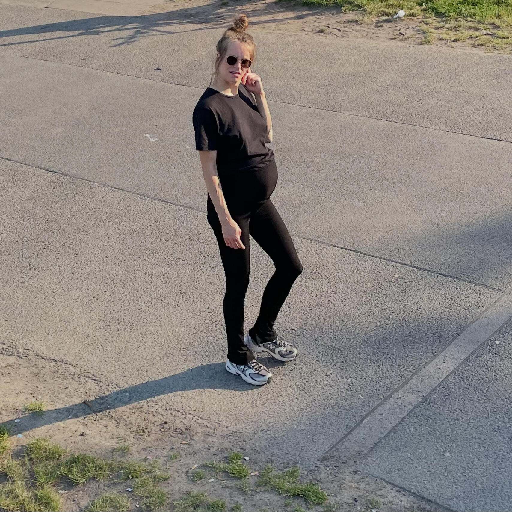 Von oben gesehen: Schwangere Frau in schwarzer Kleidung, die an einem sonnigen Tag über Beton läuft.