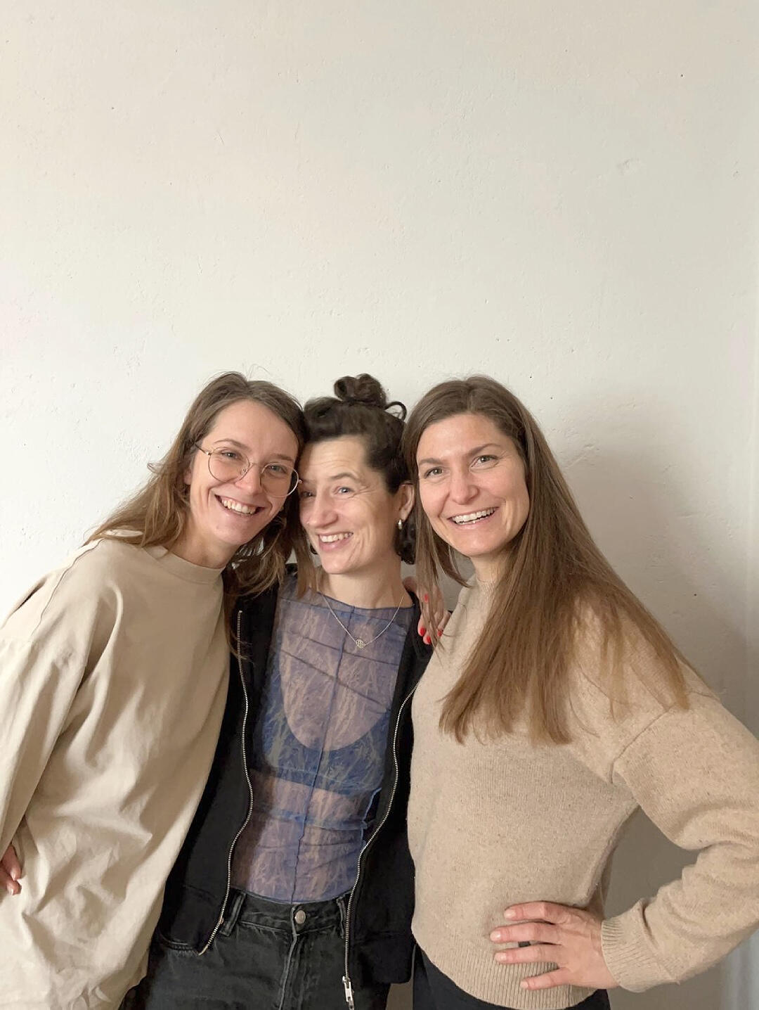 Working with Hanna: Good vibes only Three women (Antonia & Caecilia from MIUMI and Hanna Stutzki) stand close together and laugh cheerfully. They are dressed casually and stand in front of a plain white background. The image conveys a feeling of happiness and friendship.